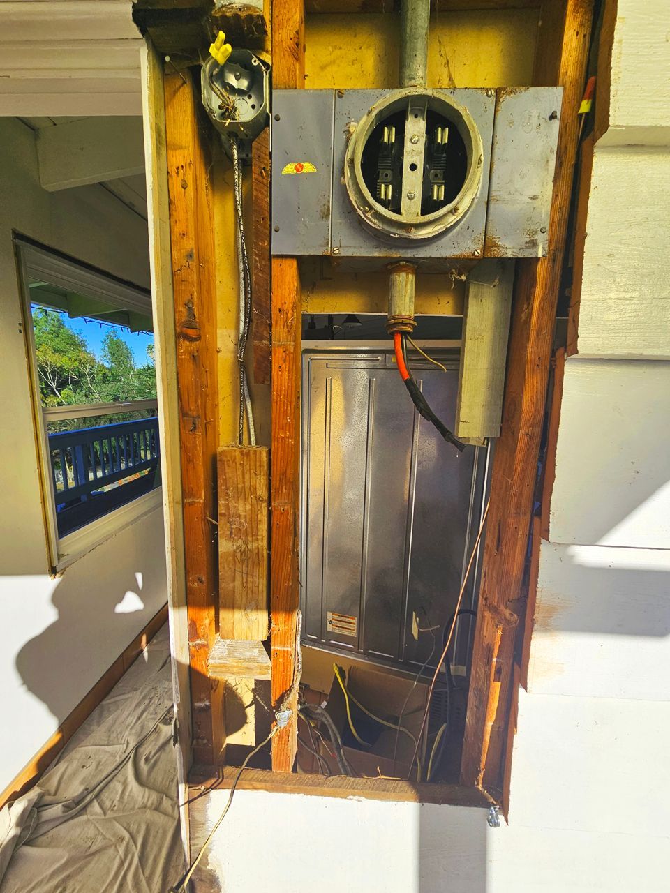 Electrical panel box in wall cavity, wires exposed. Wooden framing surrounds the metal box.
