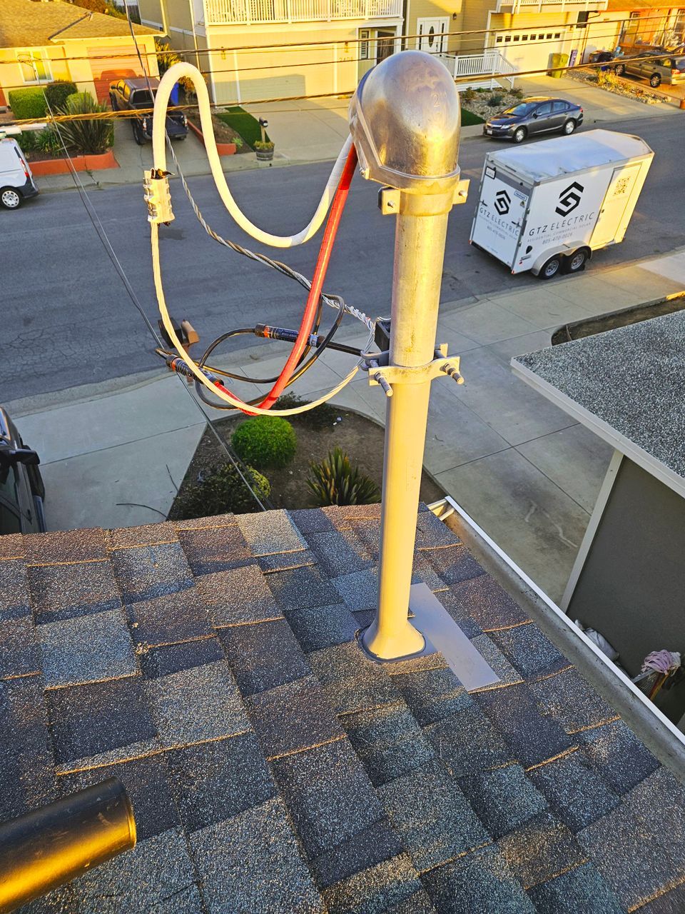 Antenna mounted on a rooftop with attached wires and tubes, possibly for communication, with a trailer in the background.