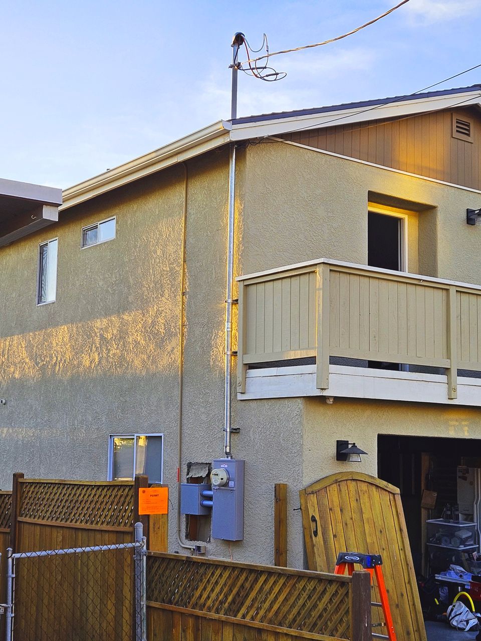 Two-story house with tan stucco, a wooden deck, and a wooden fence. A utility box is on the side.