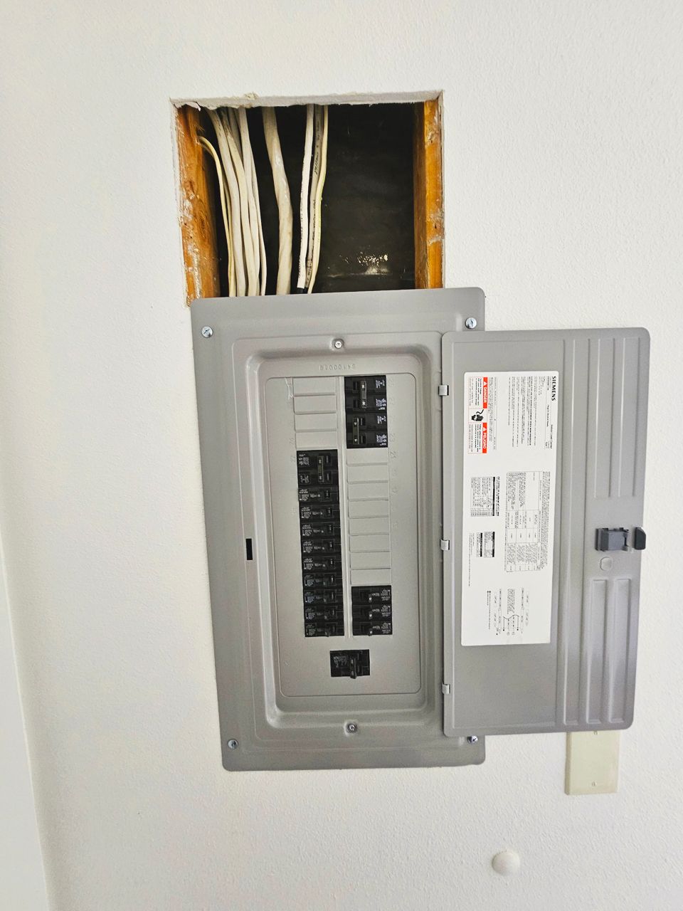 Open electrical panel in a wall, wires exposed above.