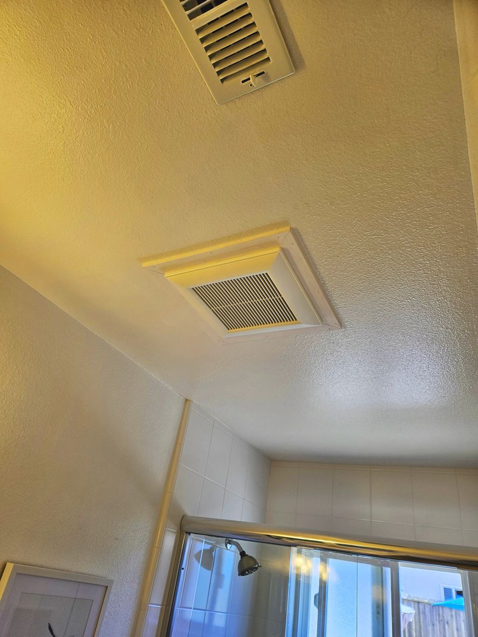White bathroom ceiling with two vents: one slotted, one square. Shower visible below.