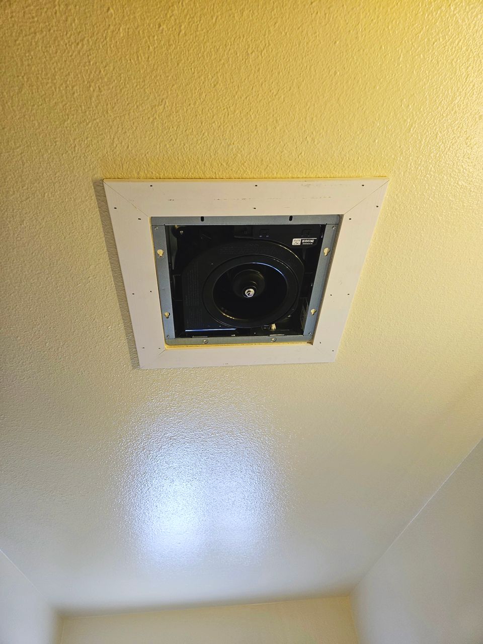 Ceiling-mounted exhaust fan with a white frame; centered on a yellow-painted ceiling.