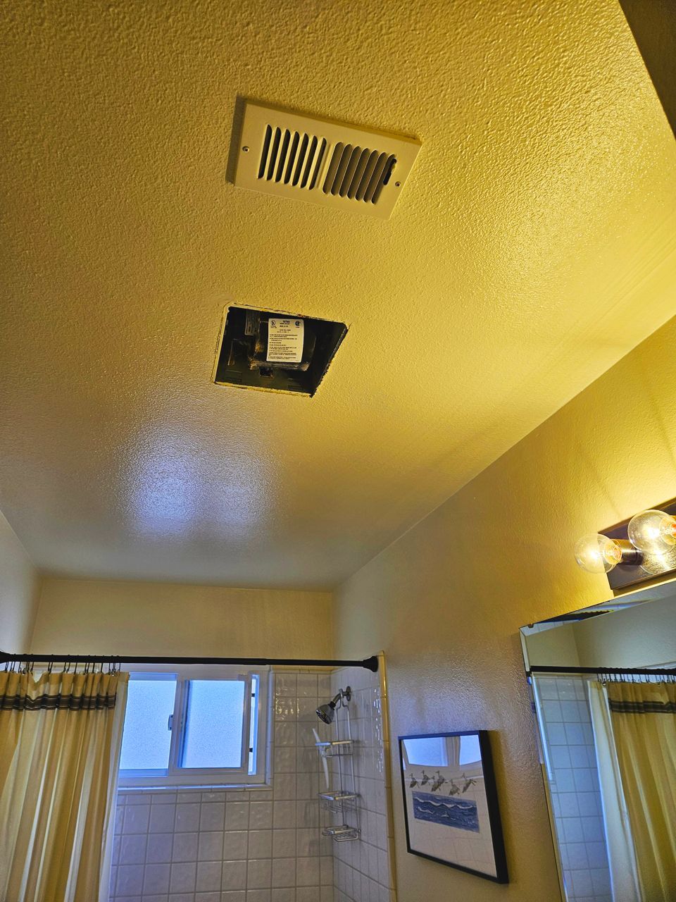 Bathroom ceiling with vent and open square, yellow walls, and shower curtain.