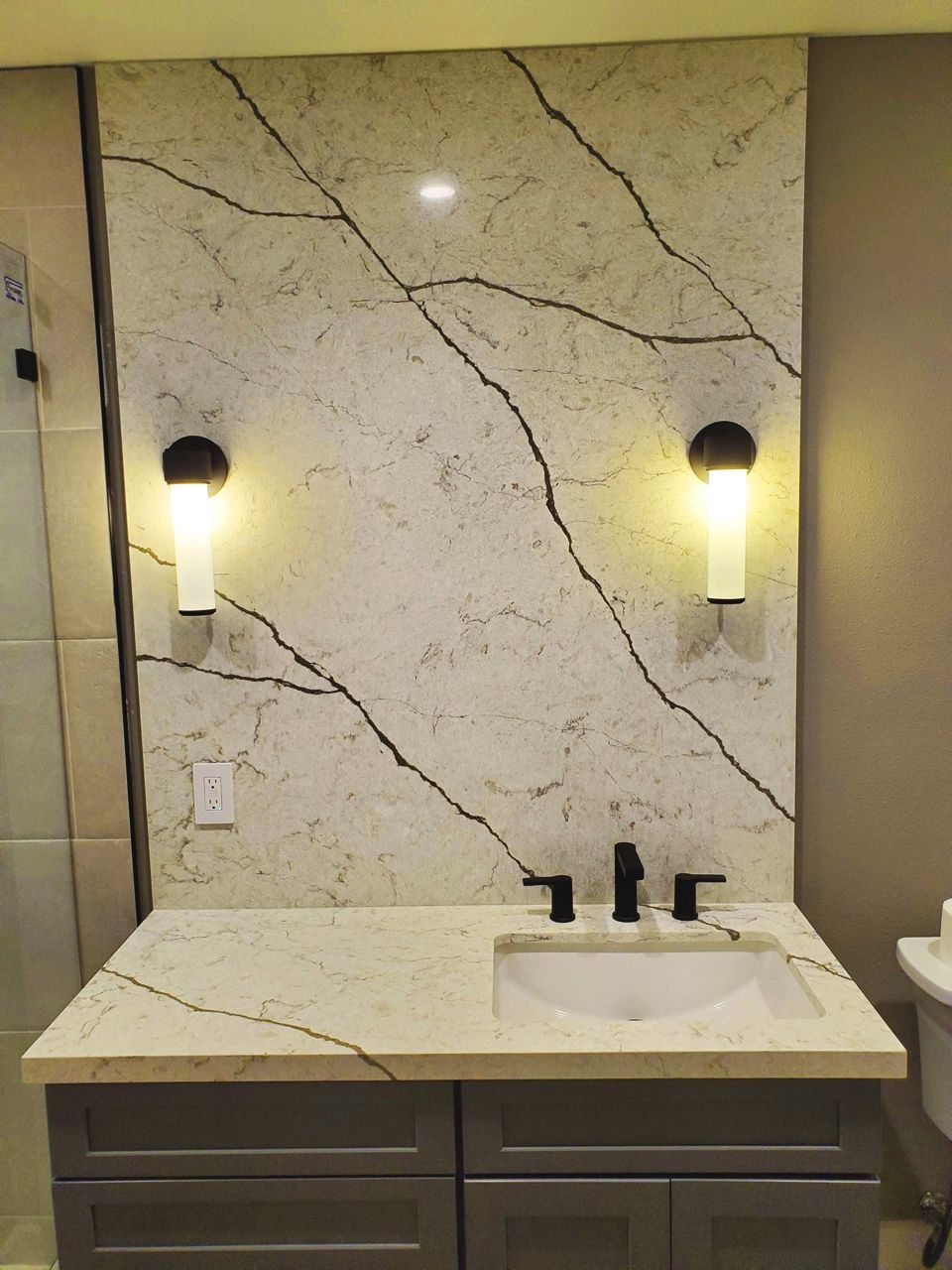 Bathroom vanity with a gray cabinet, a white sink, and a marble-like backsplash with black veining.