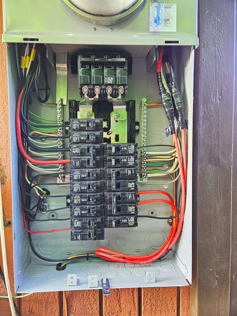An open gray electrical panel with various colored wires and circuit breakers.