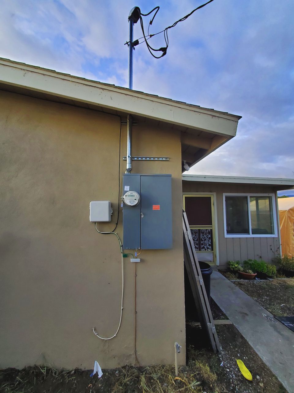 Electrical meter box mounted on a stucco wall. Conduit and power lines visible. Sunny day.