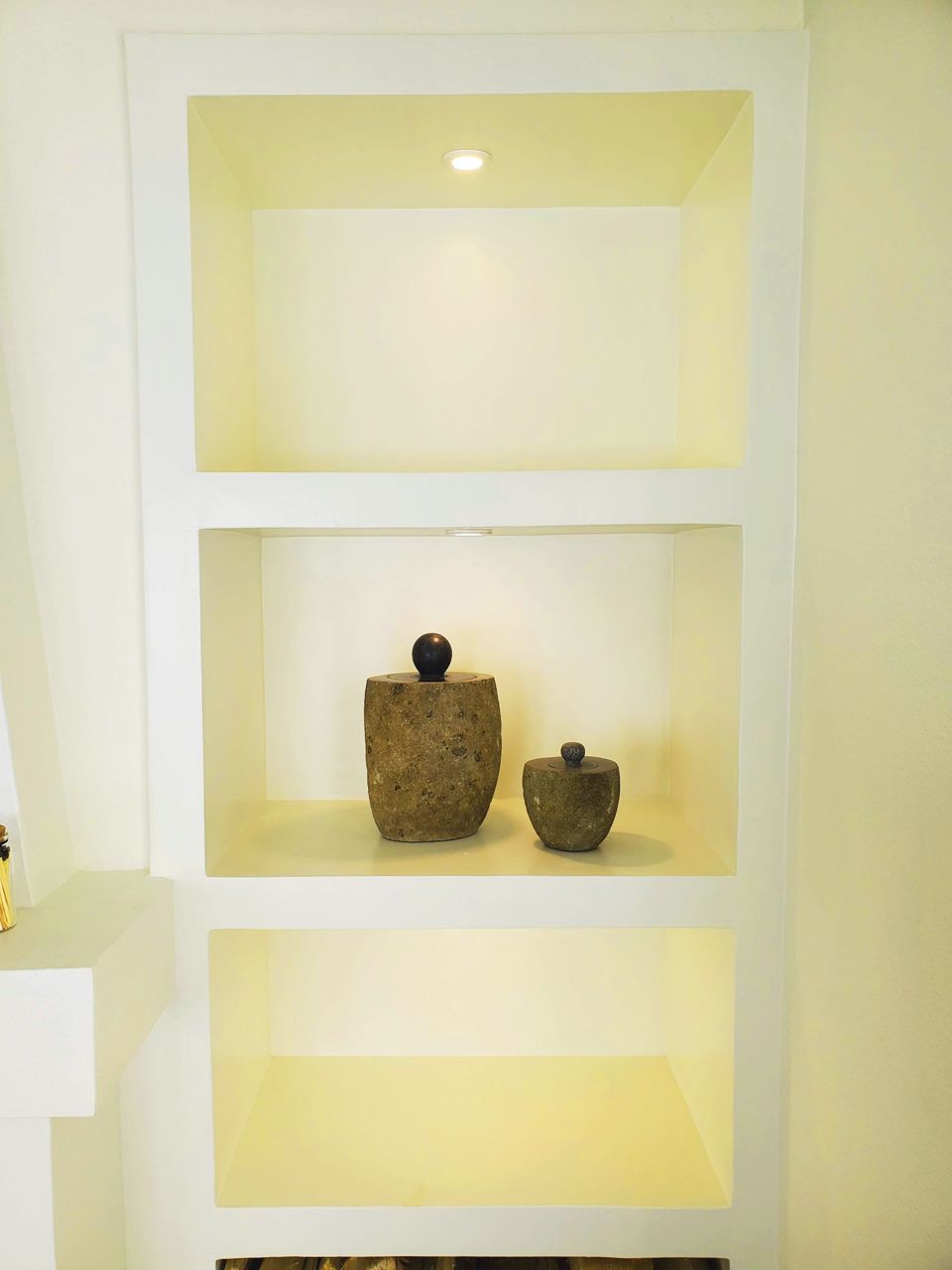 Built-in white shelves with a recessed light in the top section. Two stone objects sit on middle shelf.
