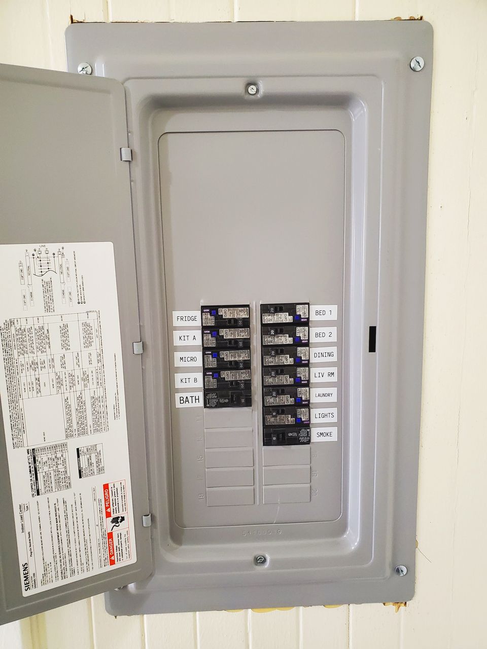 Gray electrical panel with open door, labels visible, mounted on a wall.