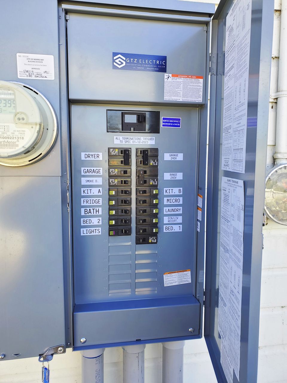 Exterior electrical panel with circuit breakers, partially open door, and electrical meter.