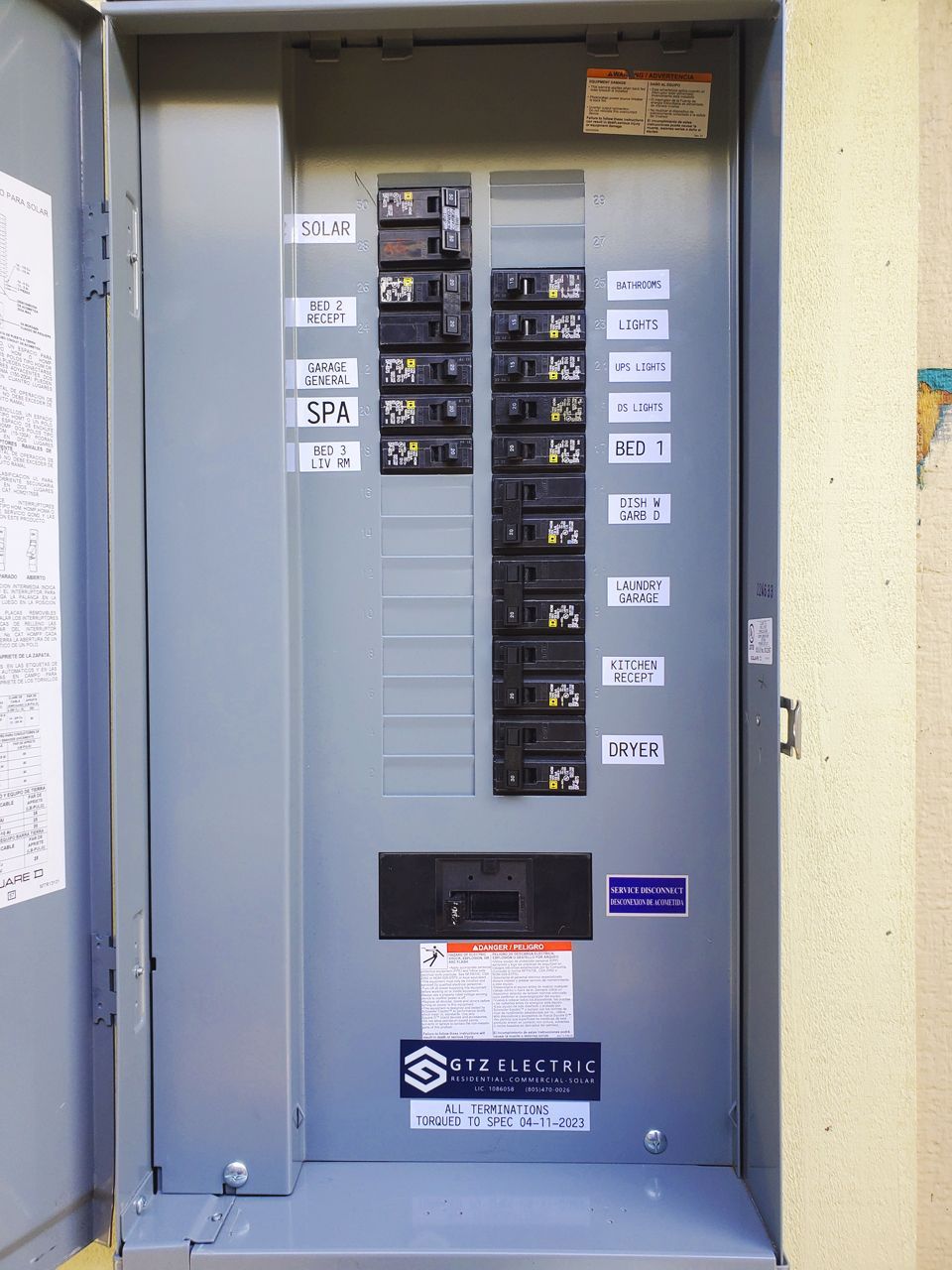 Electrical breaker box with labeled circuit breakers in a metal enclosure.