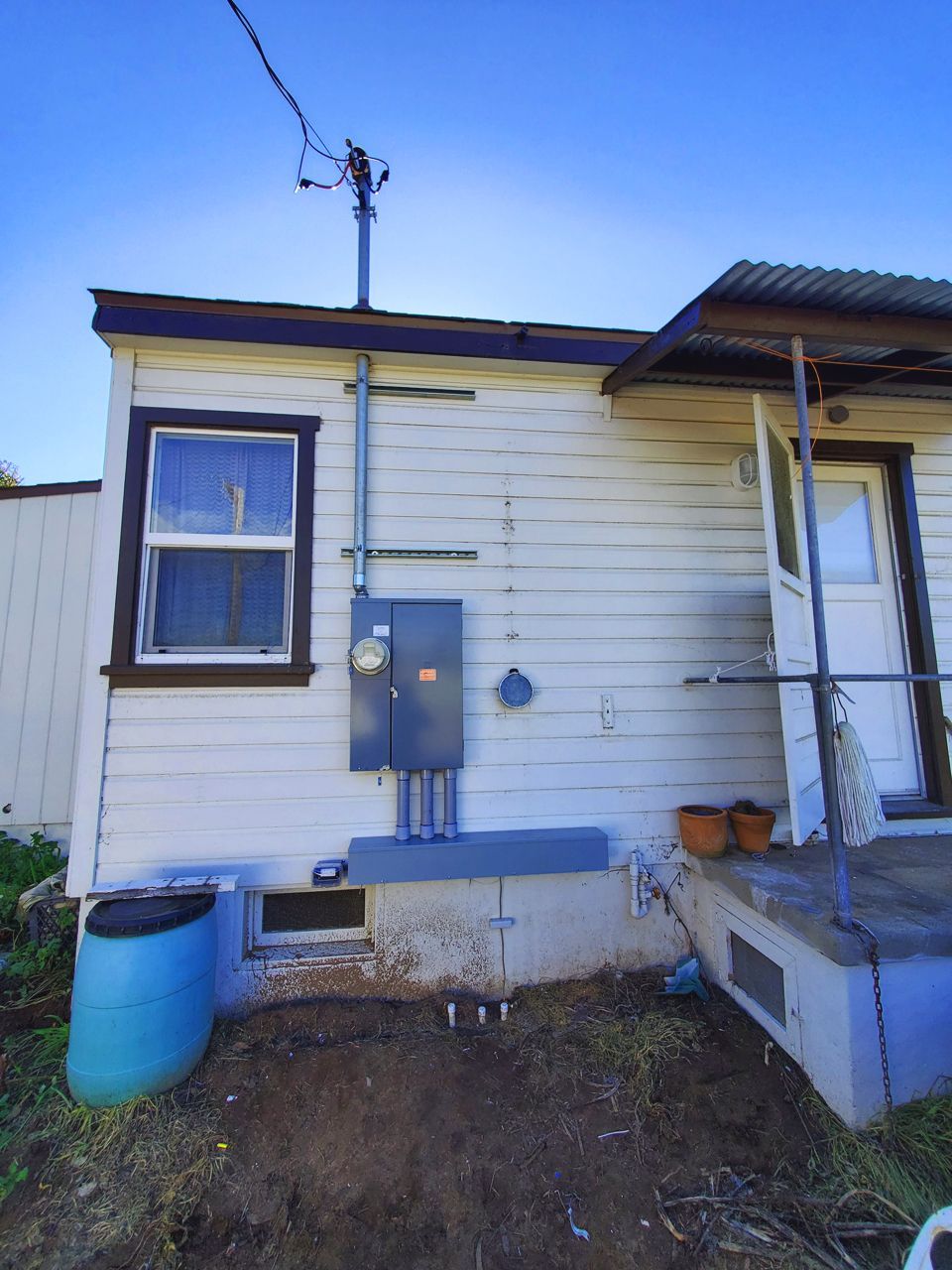 Exterior of a white house with electrical equipment: meter, panel, conduits, and a window.