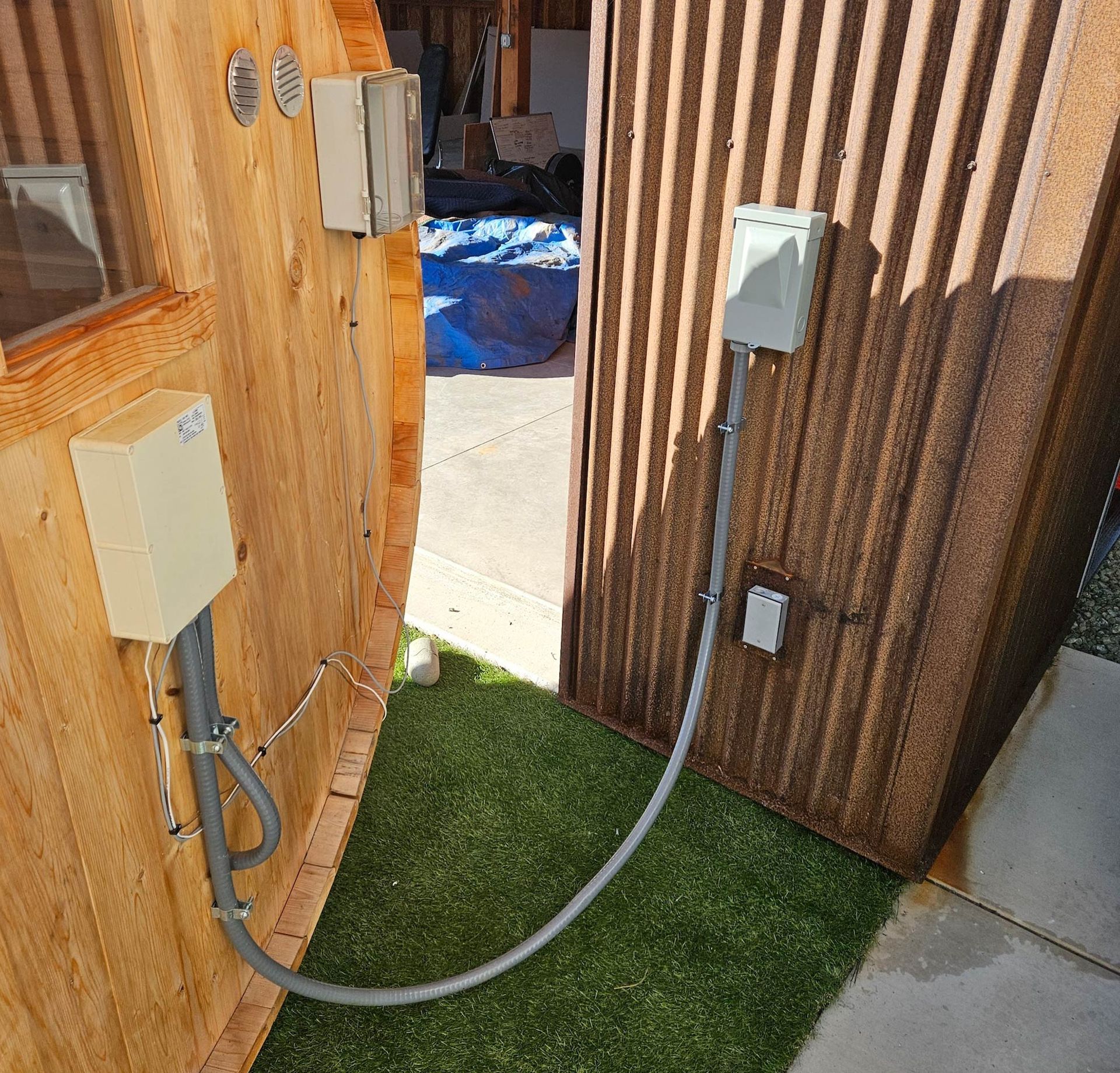 Electrical boxes and conduit on wooden and corrugated metal structures, outdoors with green turf.
