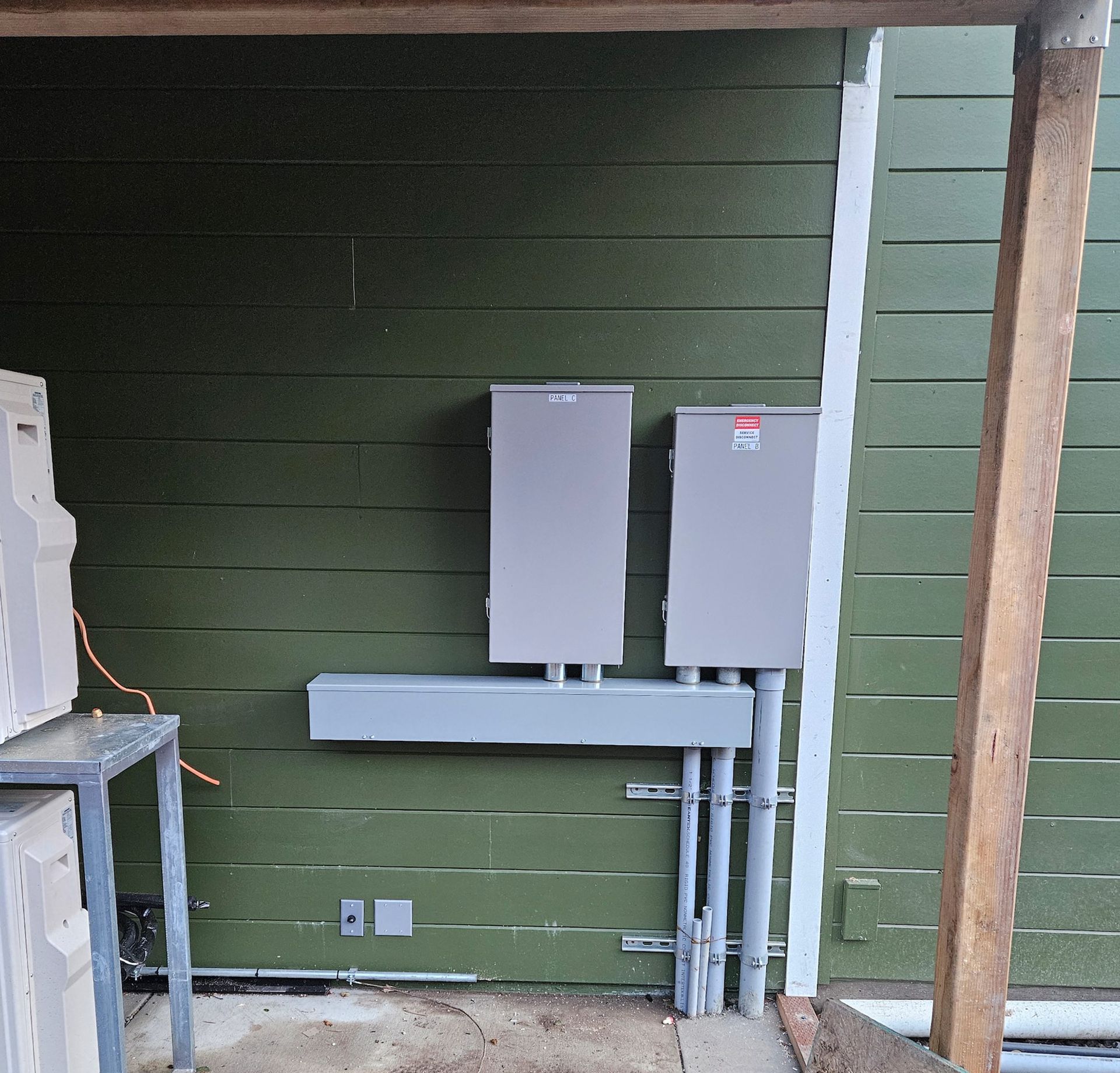 Two gray electrical boxes mounted on a green wall with conduit pipes.