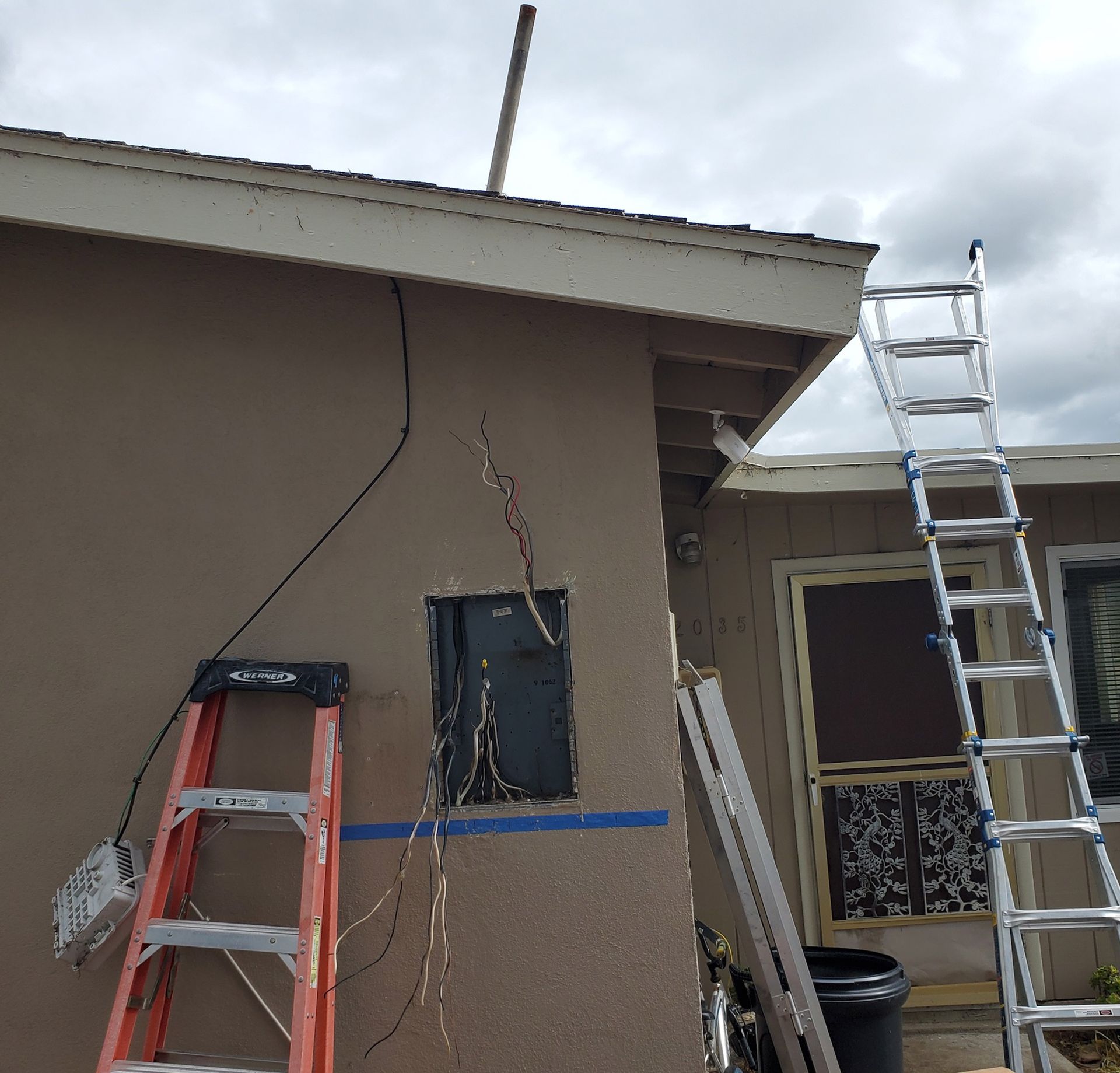 Exterior of a building with ladders, electrical wires, and an open section of wall.