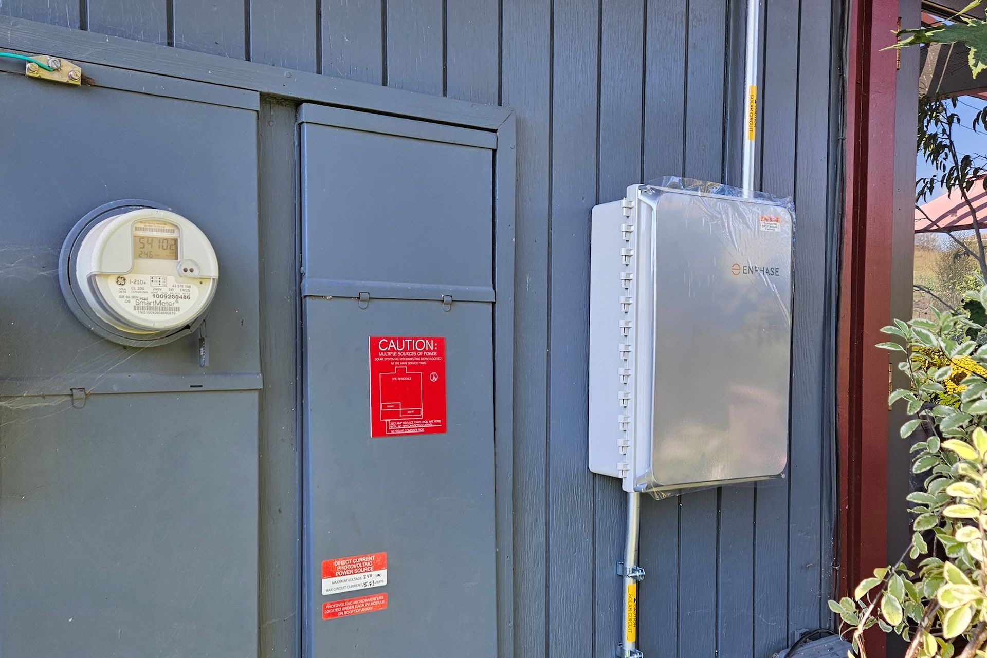 Gray electric box with meter, utility box, and conduit mounted on a gray wooden wall.