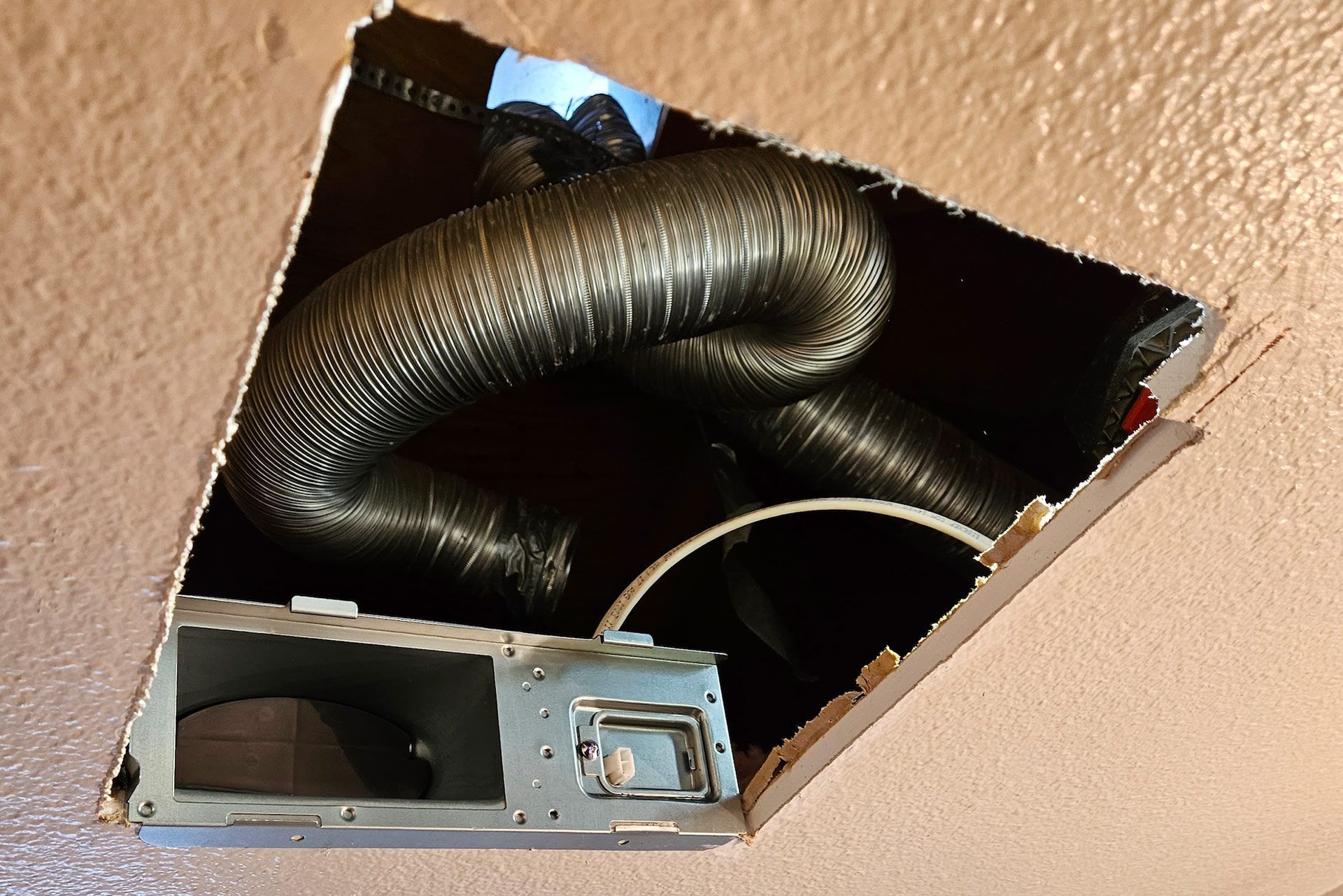 Ceiling vent with flexible ductwork visible. Black ducting within a damaged, open ceiling.