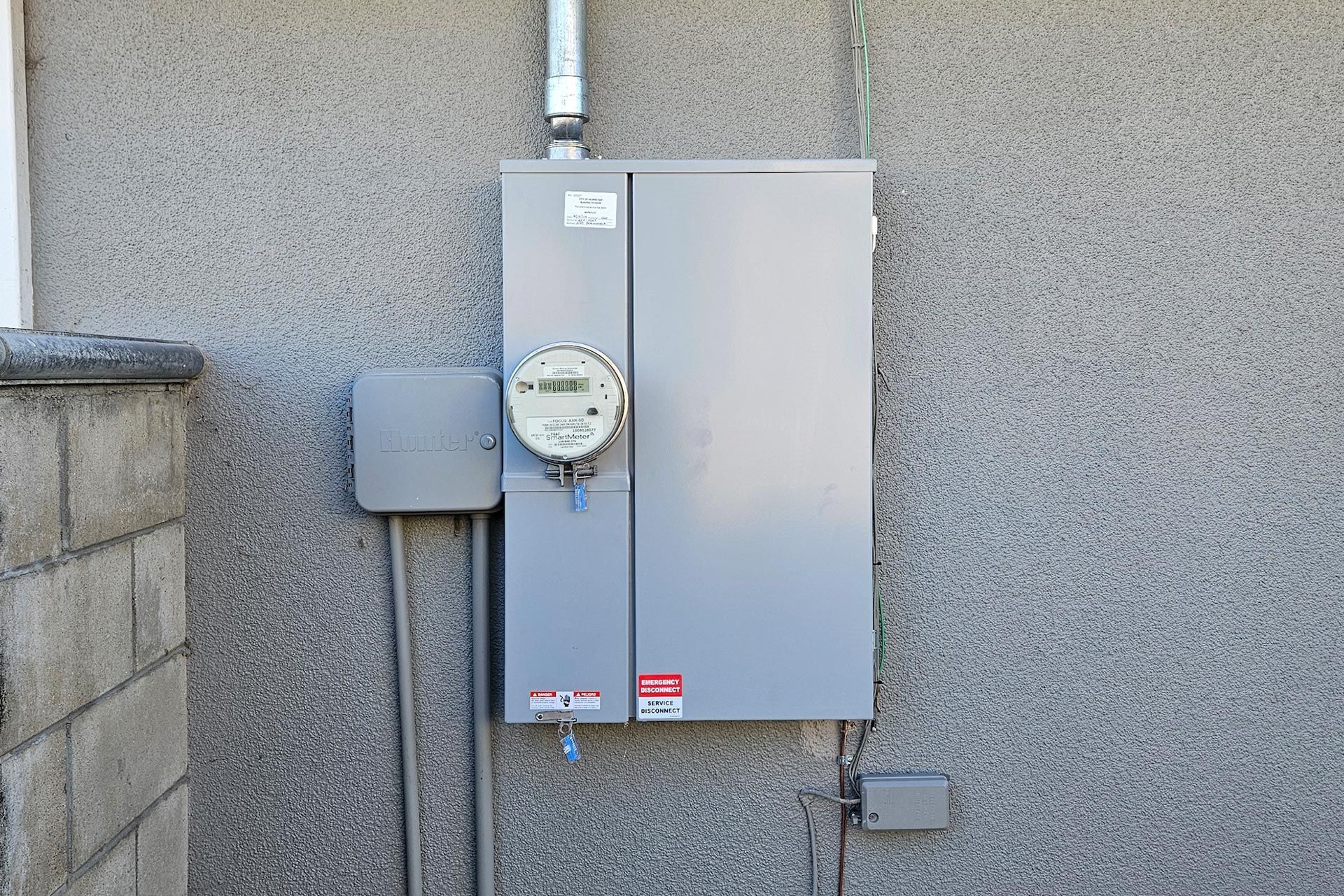 Gray electrical meter and panel on textured exterior wall.