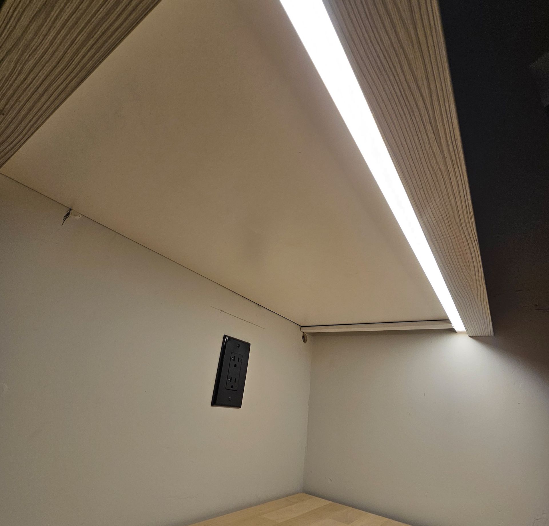 Interior view of a built-in cabinet with a bright LED light fixture installed on the underside of a shelf.
