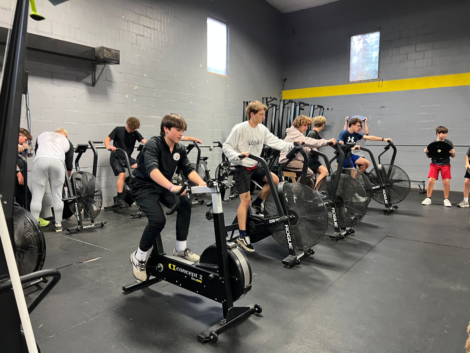 A group of young men are riding exercise bikes in a gym.