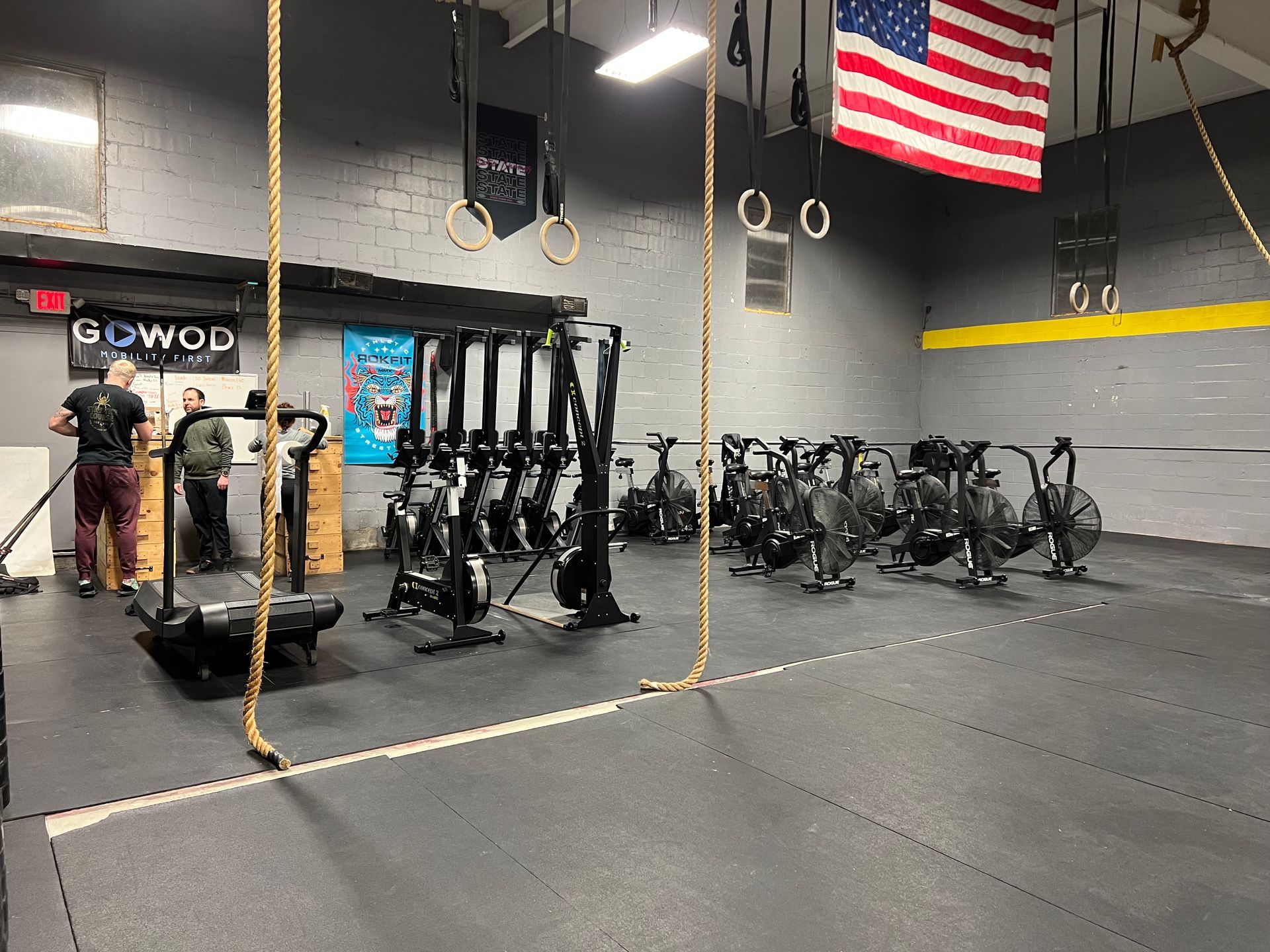 A gym with a lot of exercise equipment and an american flag hanging from the ceiling.