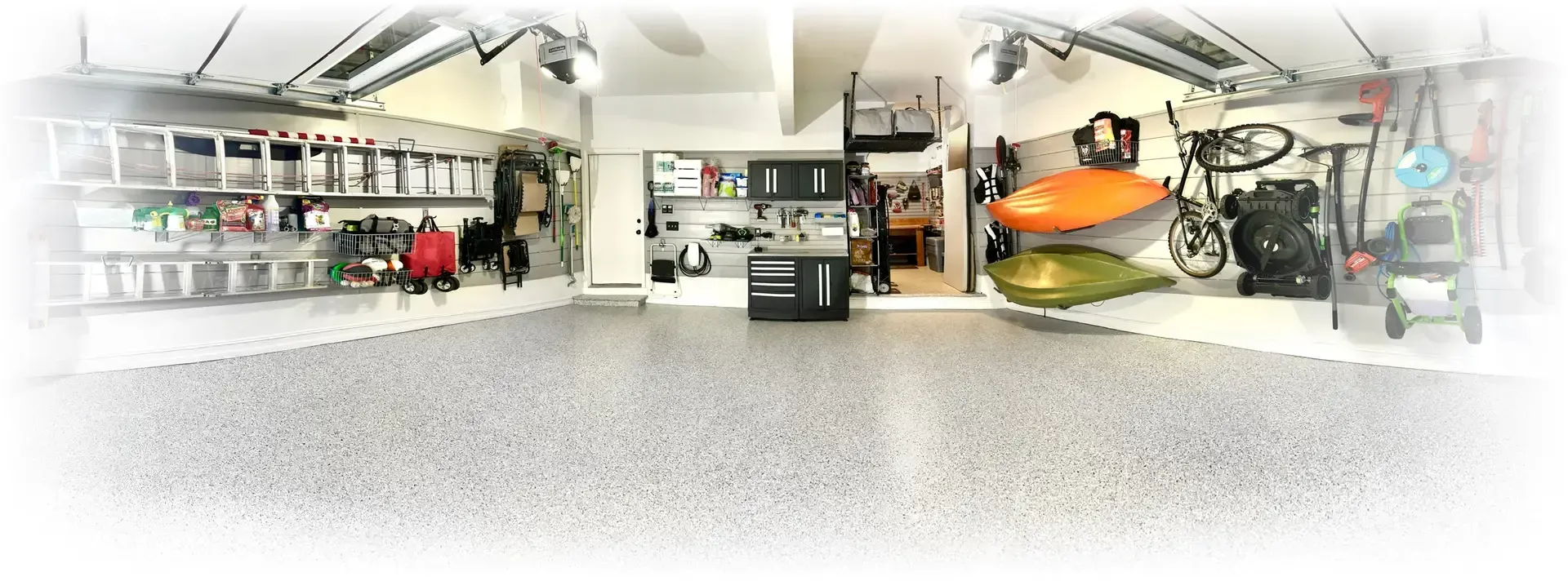 Garage interior, organized with shelving, equipment, and kayaks. Bright lighting with grey speckled floor.
