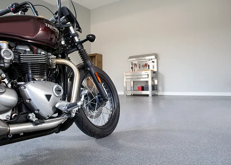Motorcycle in a garage with a metallic floor and a workbench.