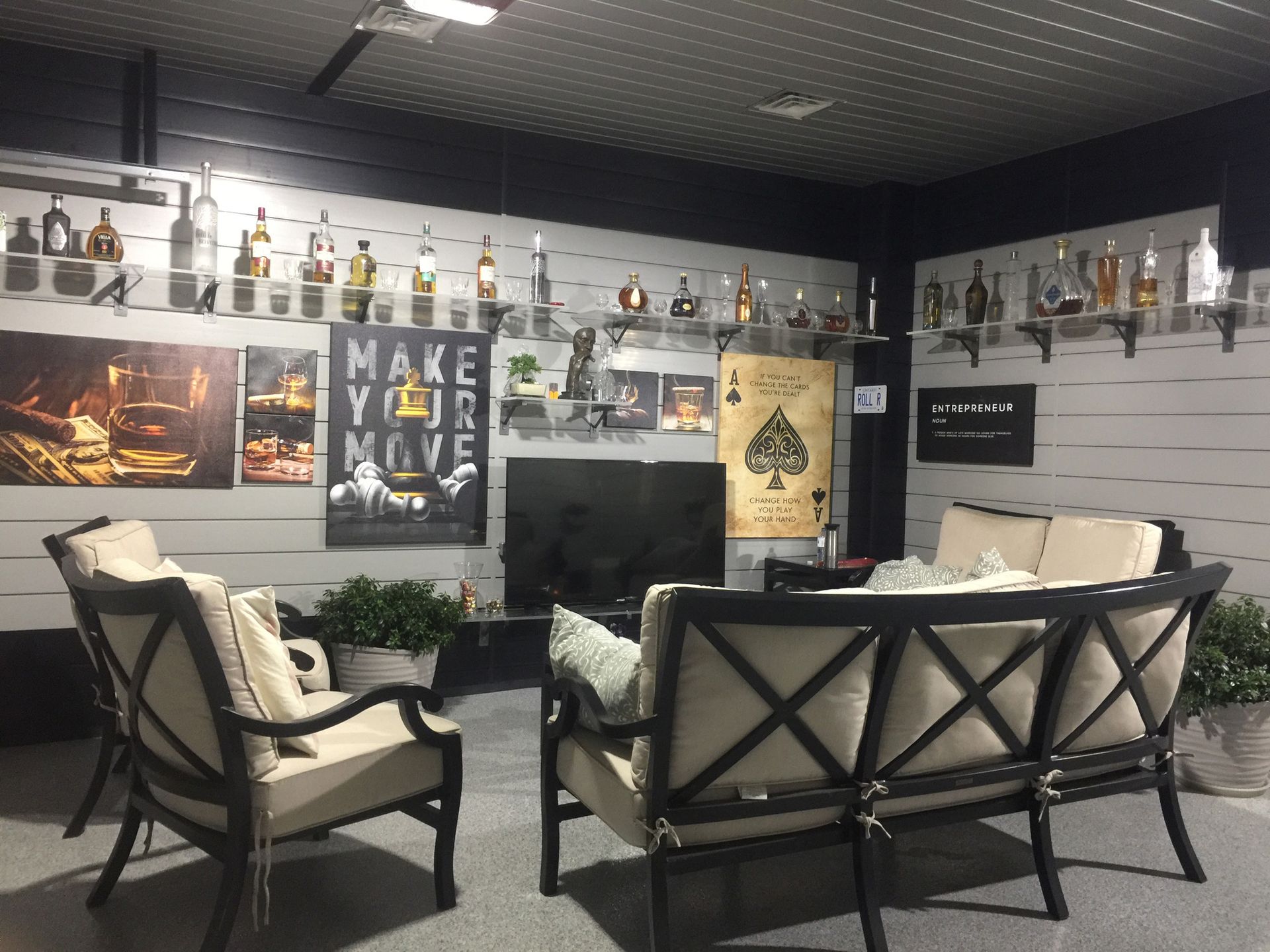 Lounge area with seating, bar with bottles, artwork, and a TV. Neutral colors, modern style, indoor setting.