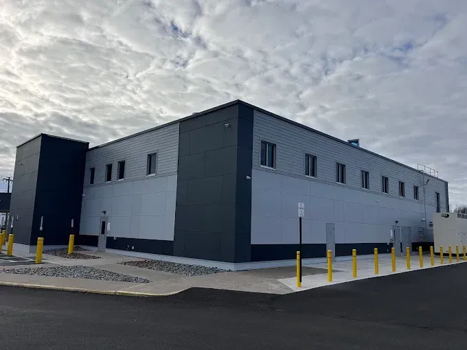 Modern two-story commercial building with light gray metal facade and large windows reflecting blue sky. Modern two-story commercial building with light gray metal facade and large windows reflecting blue sky.