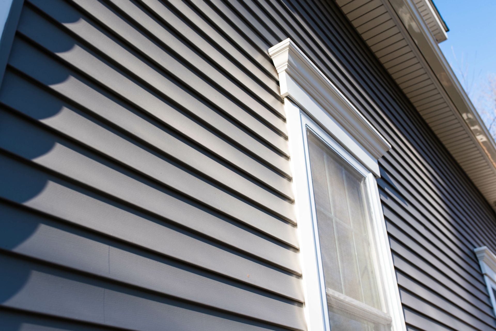 A close-up view of dark grey horizontal vinyl siding on a building with a white-trimmed window and decorative molding.