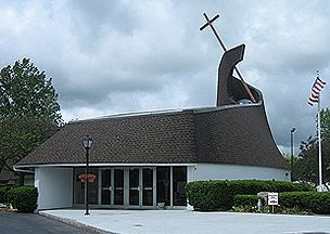 Church building with a large cross on top, under a cloudy sky.