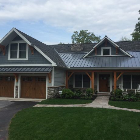 A light blue house with a gray roof and brown garage doors and accents, with a green lawn.