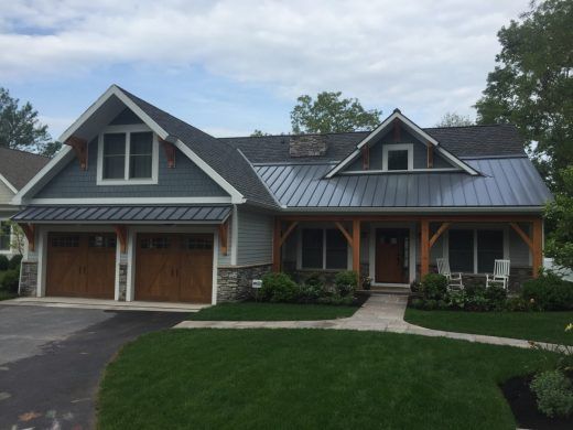 Blue house with wood accents, metal roof, two-car garage, and green lawn.