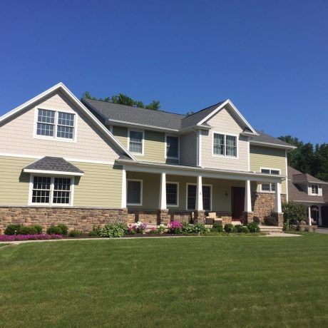 Two-story house with green siding, stone accents, and a porch, set against a blue sky.