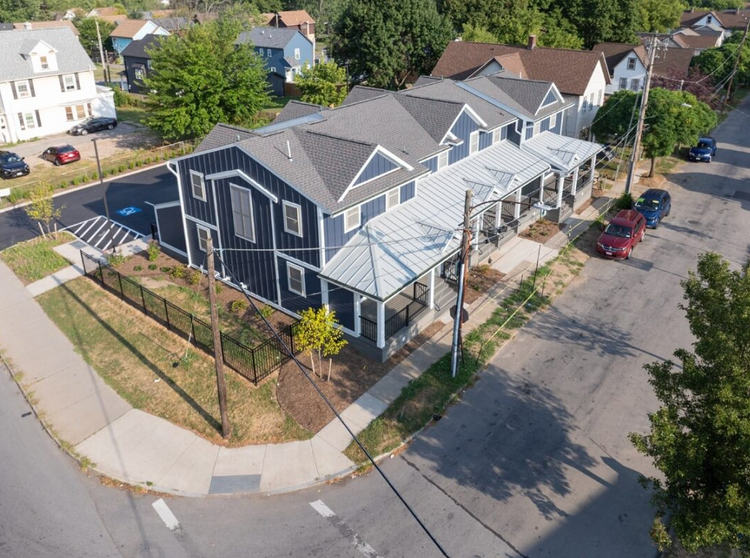 Gray and beige house exterior with multiple dormers and a blue sky.