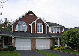 Townhouses with brick and brown siding, white garage doors, and a tree in the yard.