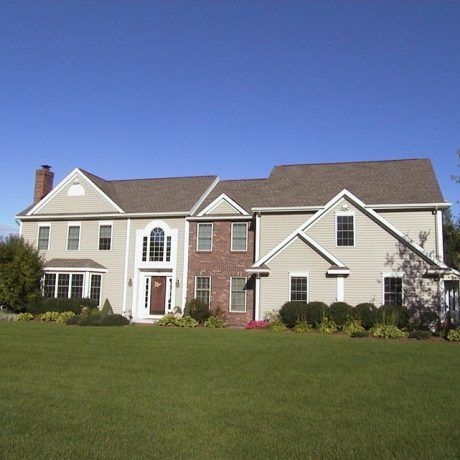 Two-story house with green lawn, brick and beige siding, brown roof, and a blue sky.