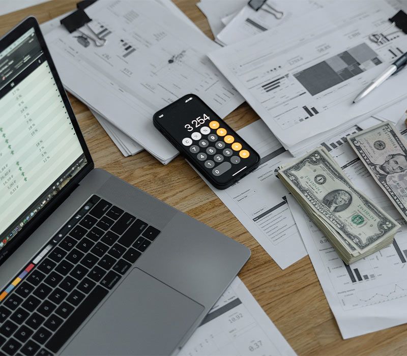 laptop on desk with calculator and cash money stacked neatly on financial papers