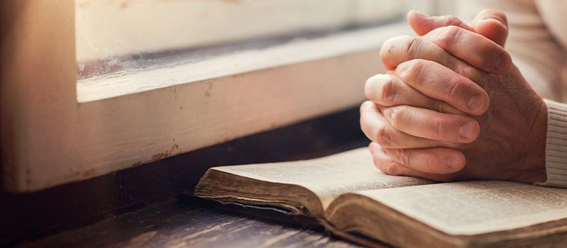 folded hands resting on open bible