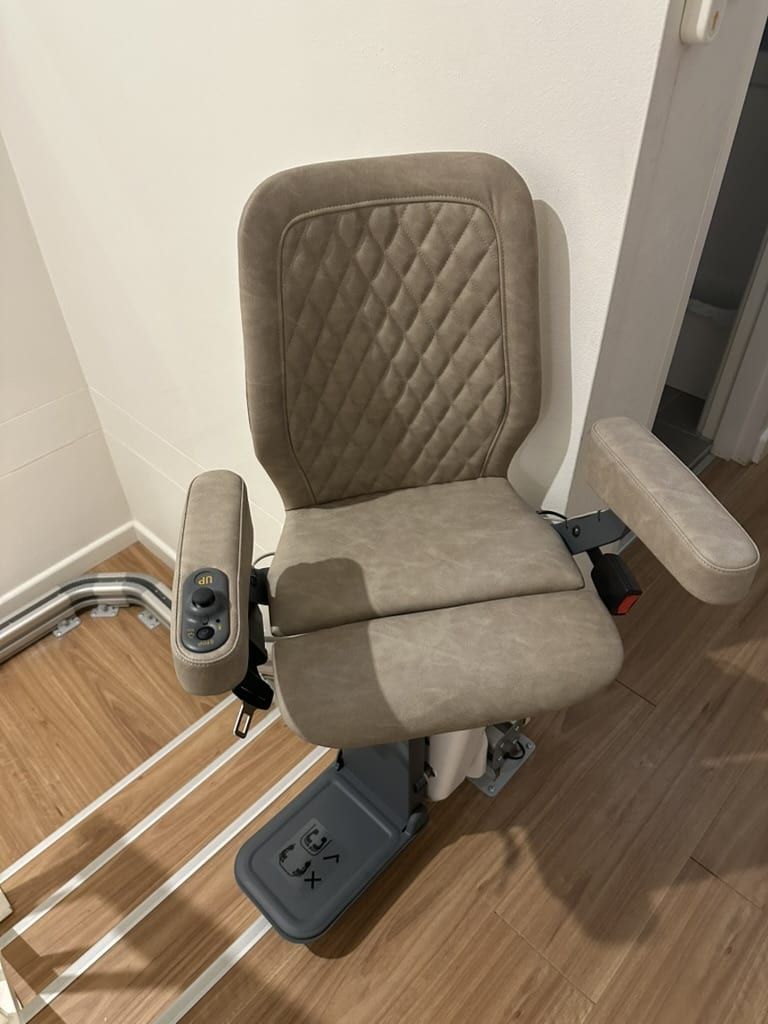 Grey padded mobility chair with armrests in a hallway, viewed from above.