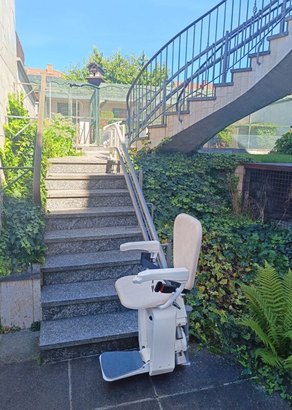 White stair-climbing wheelchair at bottom of outdoor steps beside a blue-railed staircase and greenery