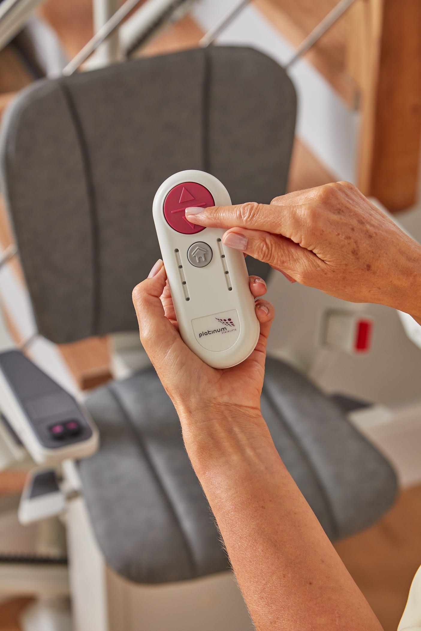 Hands using a white remote to control a gray recliner in a cozy living room