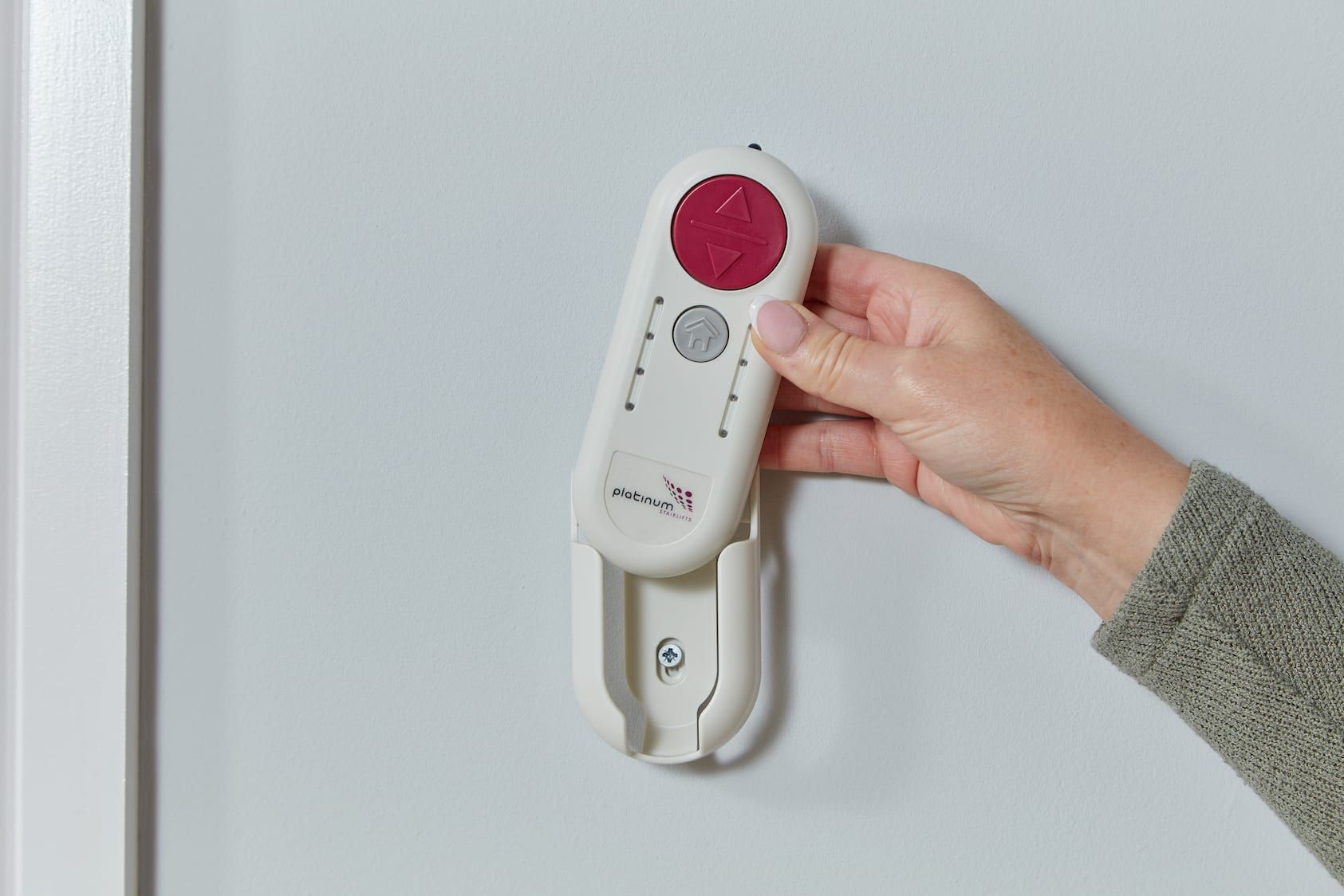 Hand holding a white wall-mounted emergency call device with a red button.