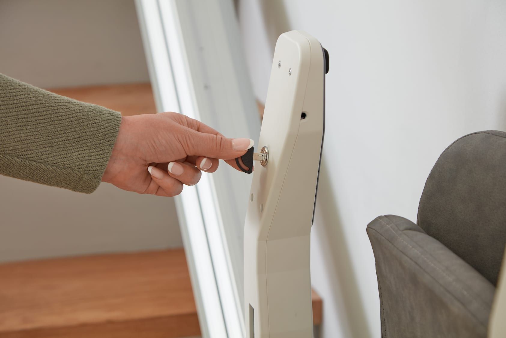 Hand turning a key in a white door lock near a gray sofa