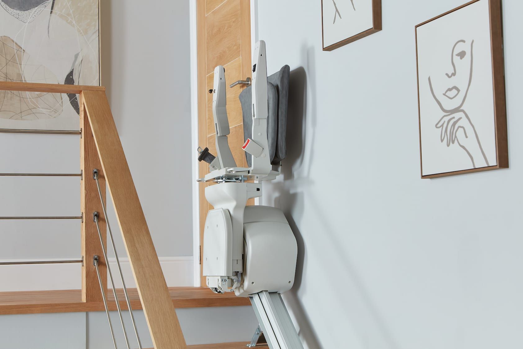 Wooden staircase beside a white wall with two framed sketches and a hanging white appliance on a wall-mounted rack