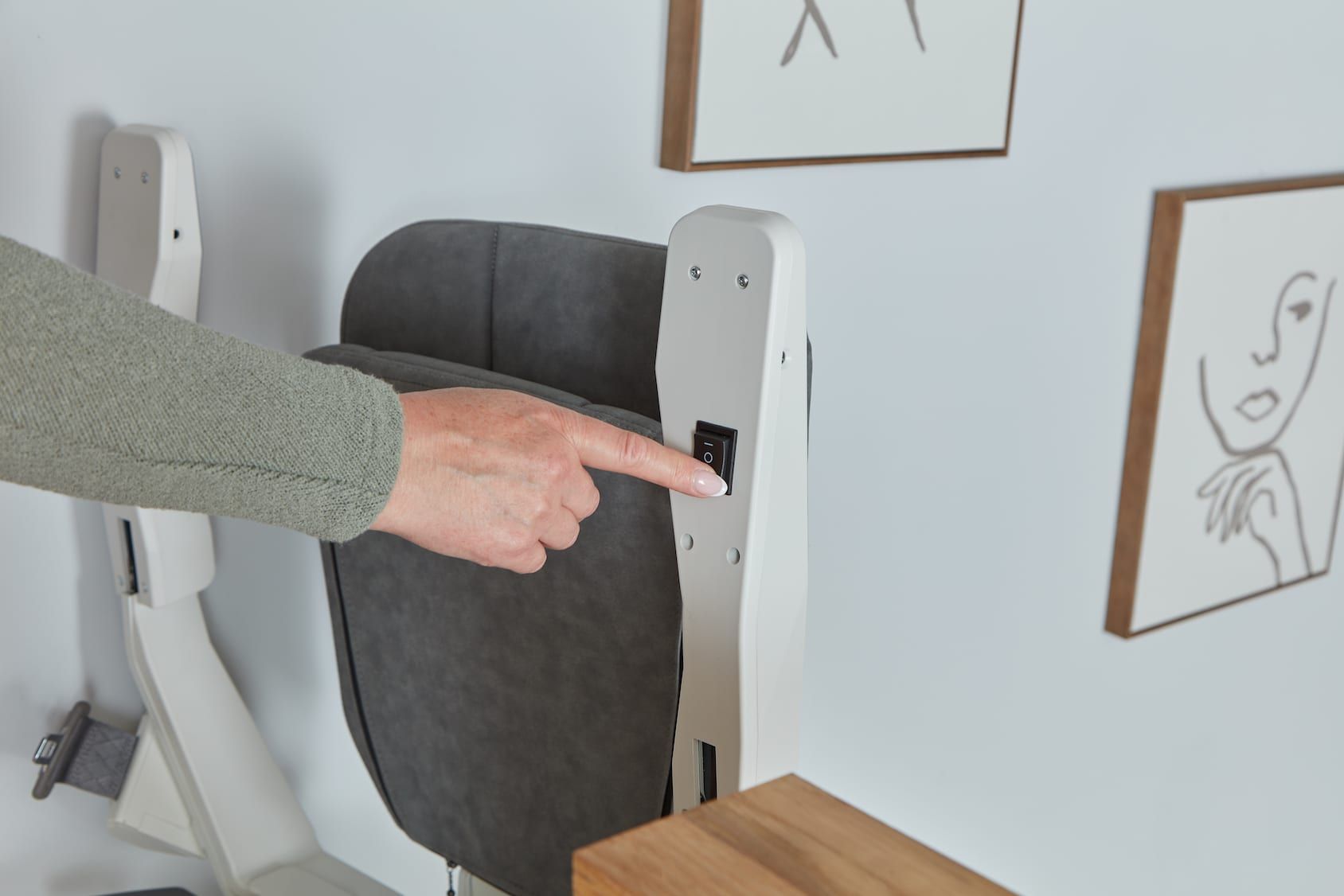 Person pointing at a white wall-mounted chair in a home interior, with framed drawings nearby