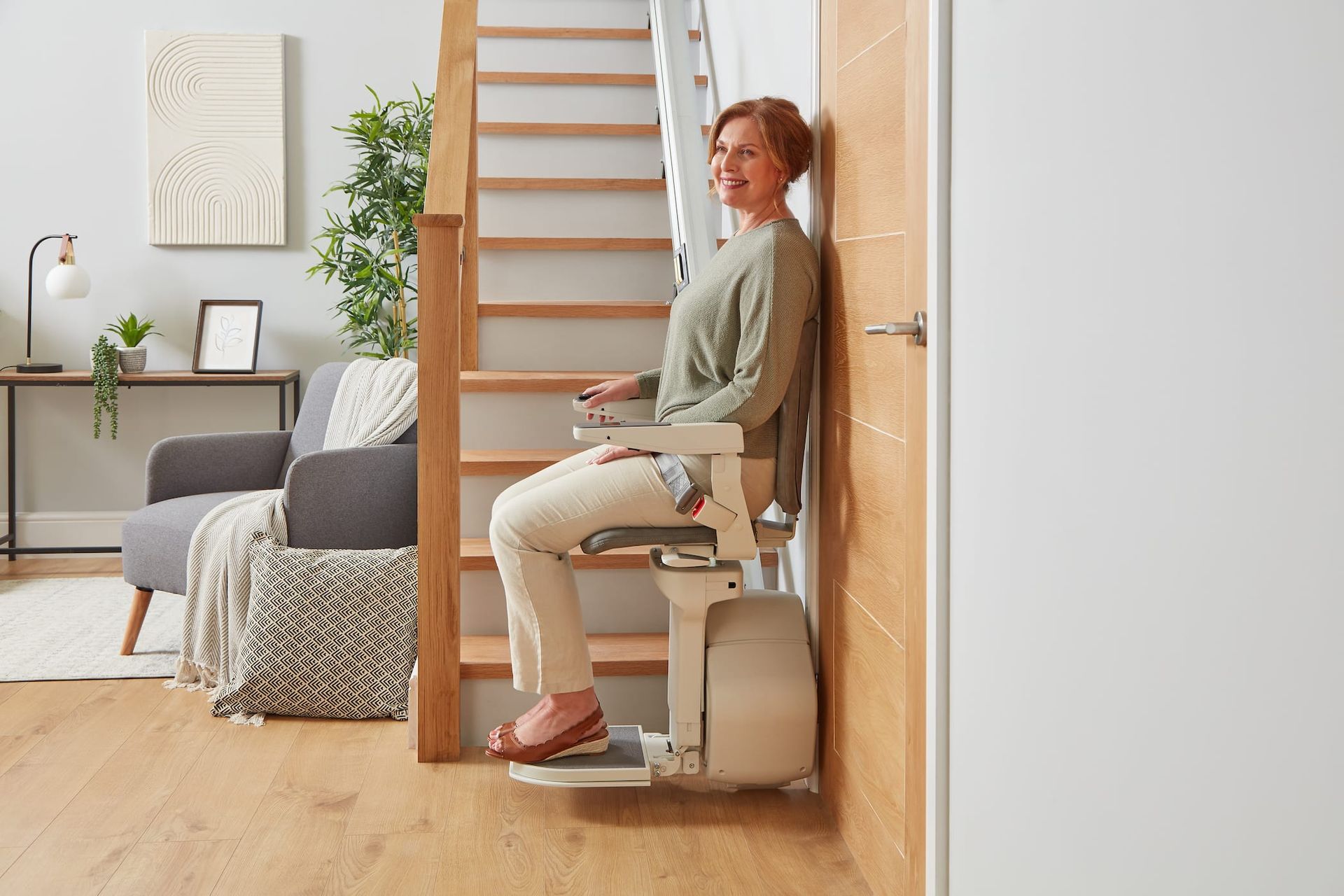 Person seated on a stairlift in a bright home interior, next to a staircase.
