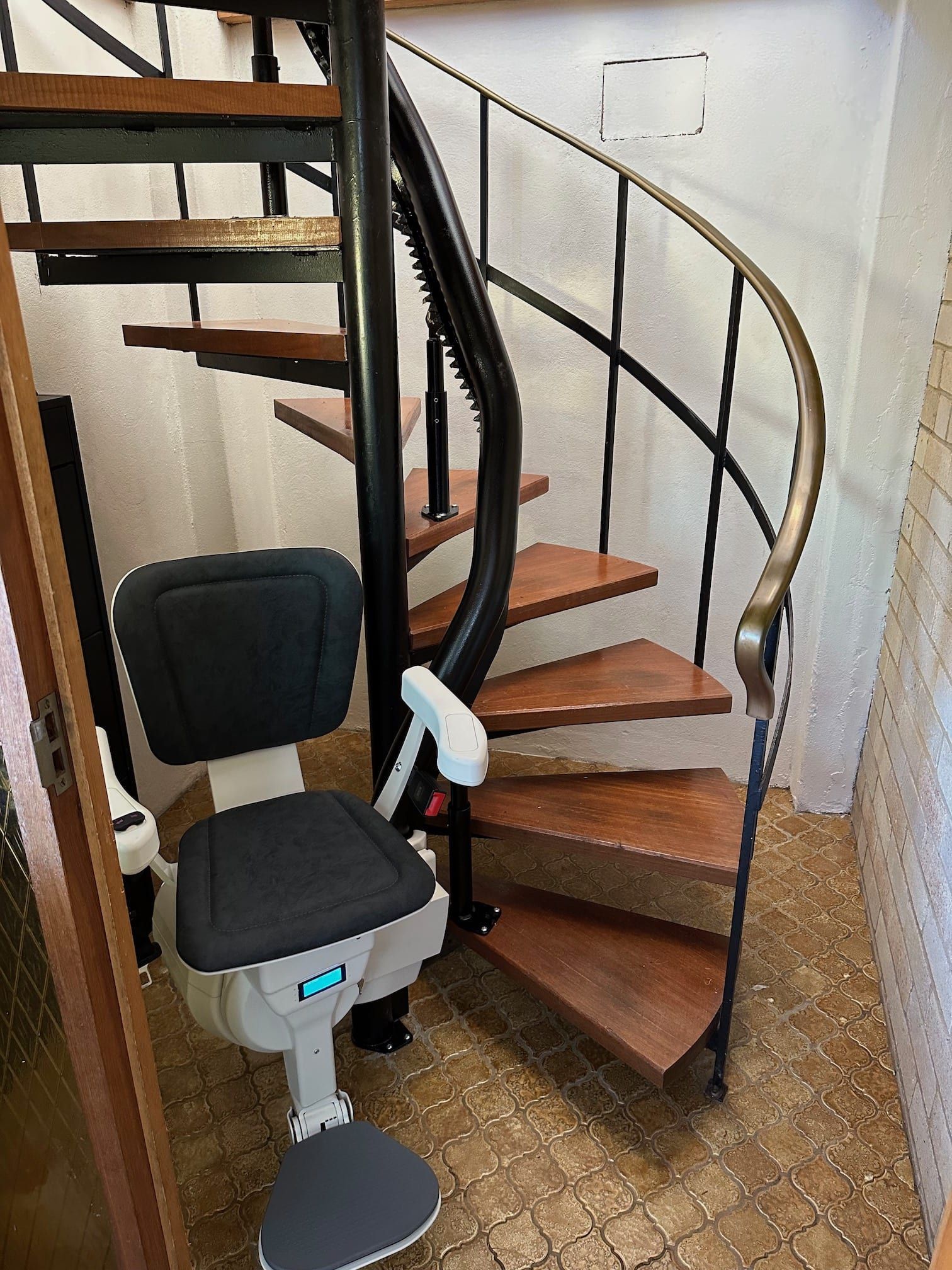 Spiral staircase with installed stair lift, brown treads, black handrail.