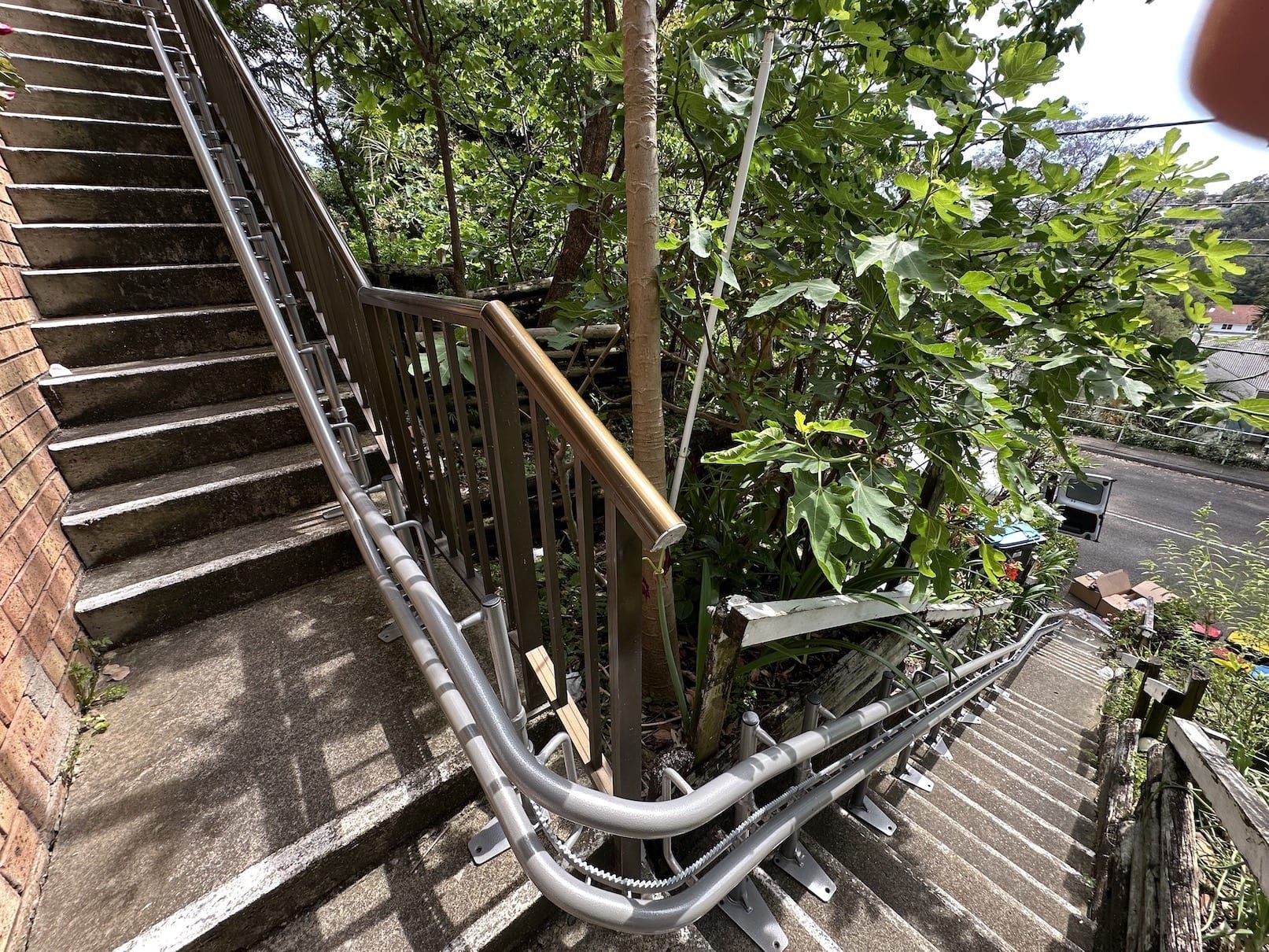 Outdoor stairway beside a brick wall with metal railings and tree-lined steps descending to a road
