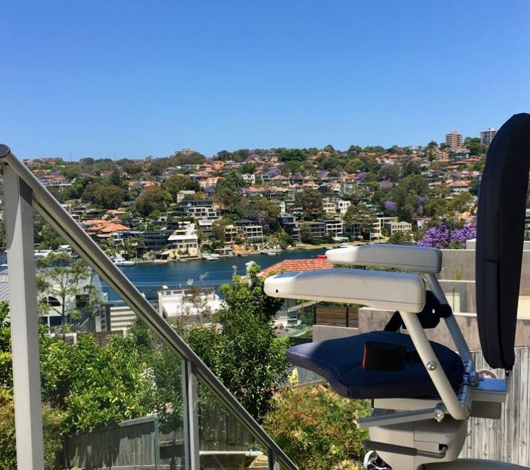 Stairlift on a deck overlooking a waterfront town. Blue sky, water, and homes visible.