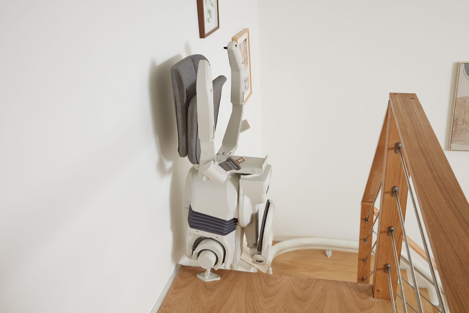 A stairlift installed on a staircase, with clothing hanging from it. White walls and wooden banister are present.
